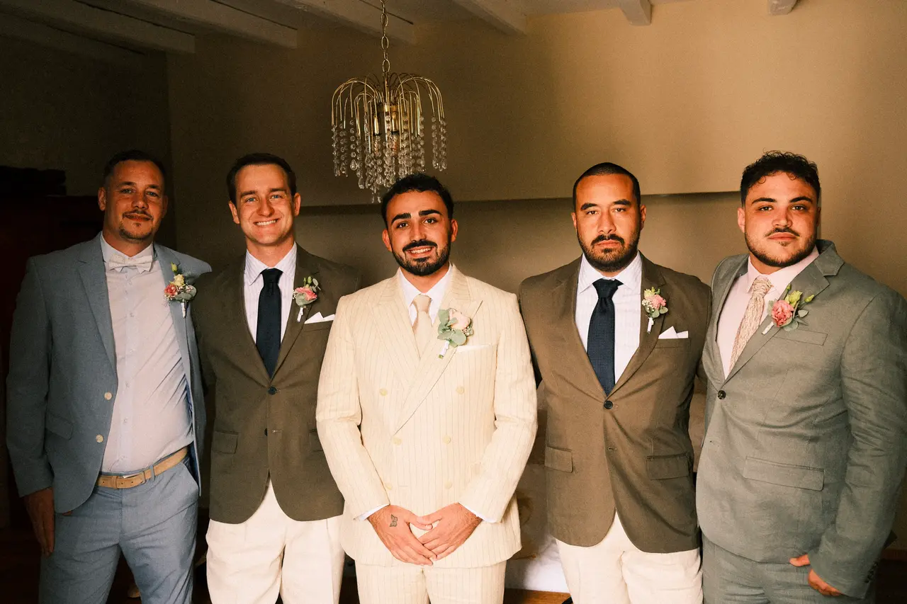 marié entouré de quatre hommes en costumes bleu, kaki et gris, chambre avec lustre