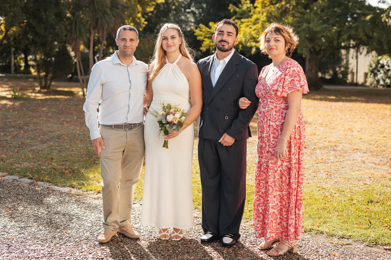 Les mariés, un invité en chemise claire et une invitée en robe rouge à fleurs