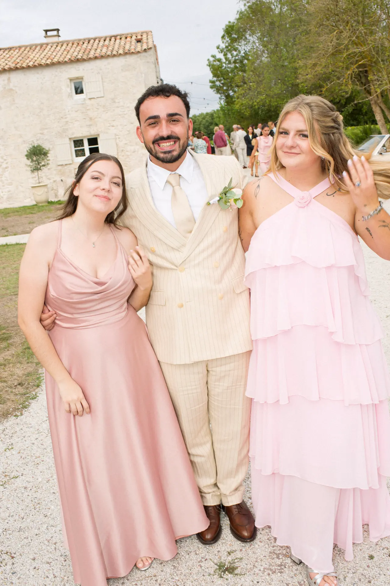 marié entre deux femmes en robes rose poudré et rose volantée, allée de gravier