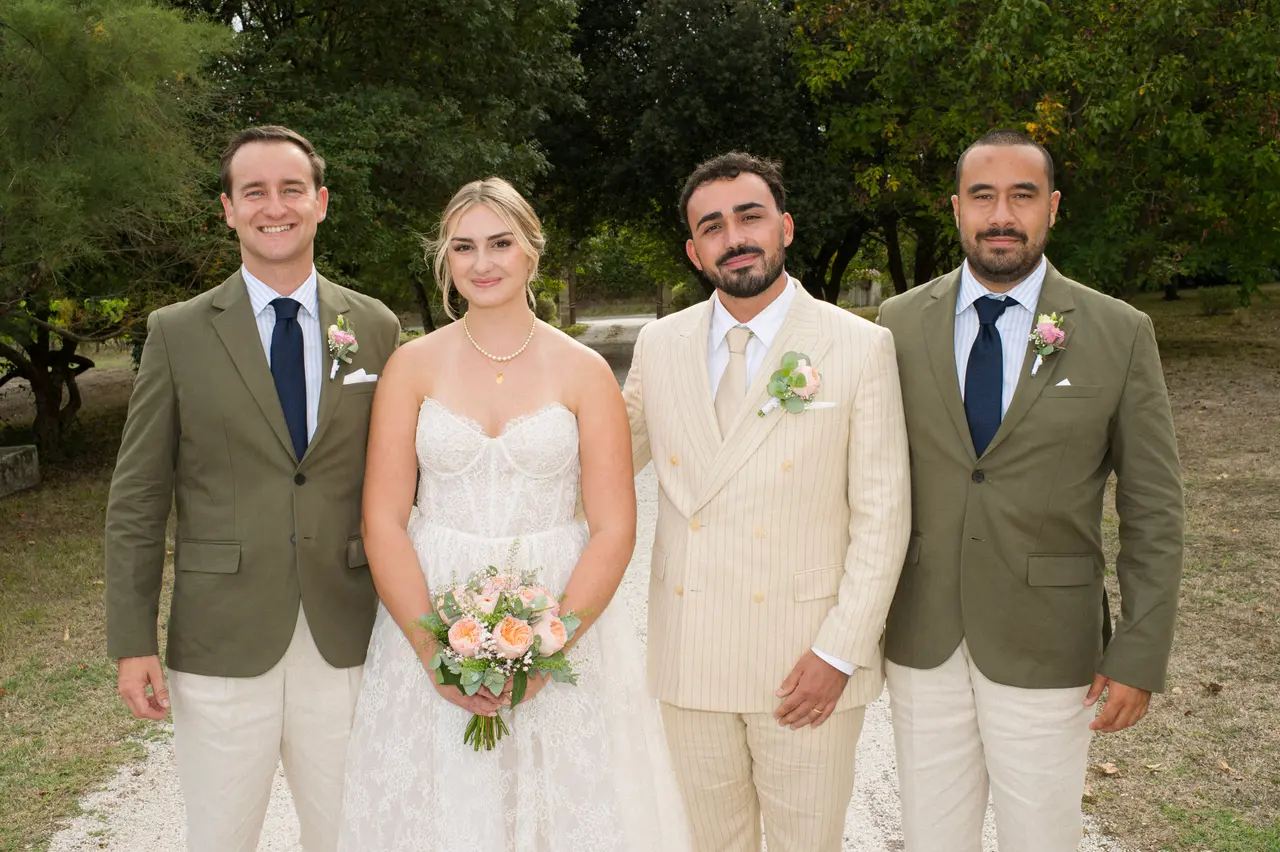 mariés encadrés par deux hommes en vestes kaki et cravates marine, parc arboré