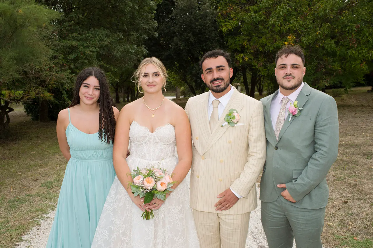 mariés entre femme en robe turquoise et homme en costume sauge dans un parc arboré