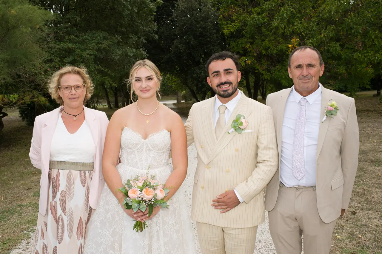 quatre personnes en ligne, femme en veste rose pâle, homme en costume beige, arbres