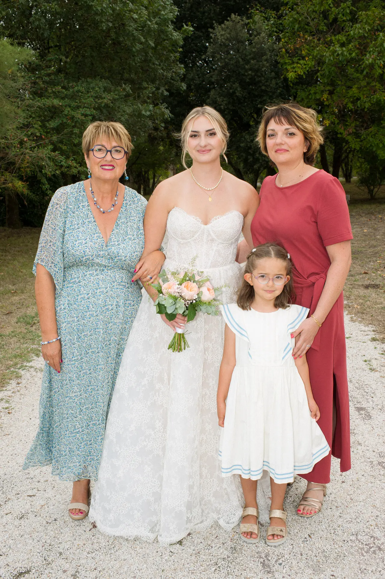 mariée avec femme en robe bleue fleurie, femme en robe terracotta et fillette en blanc, allée du parc