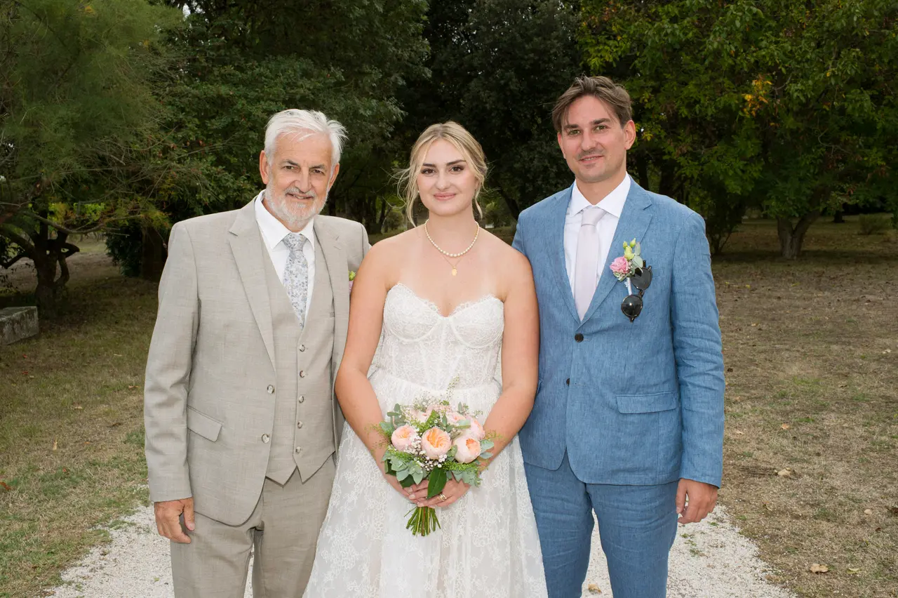 la mariée entre un homme aux cheveux blancs en costume gris et un homme en bleu