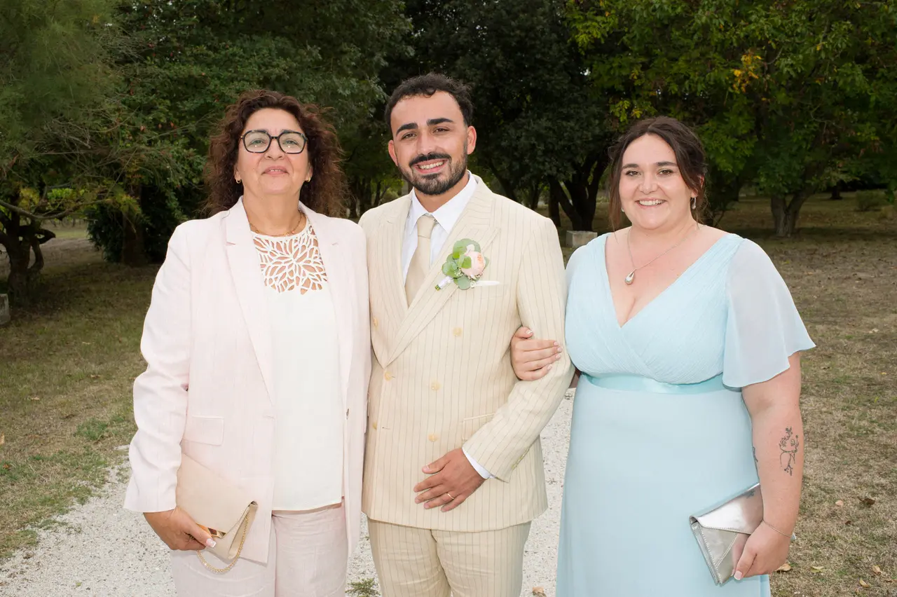 le marié entre une femme en tailleur rose pâle et une femme en robe bleu ciel