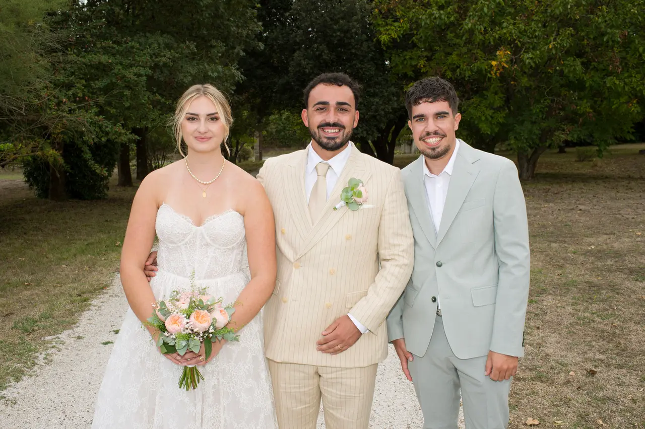 les mariés avec un homme souriant en costume vert d'eau, allée sous les arbres