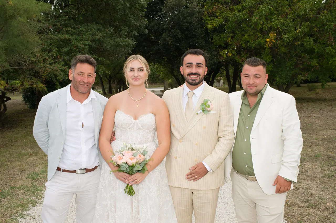 mariés entre homme en veste gris clair et homme en veste blanche, allée arborée