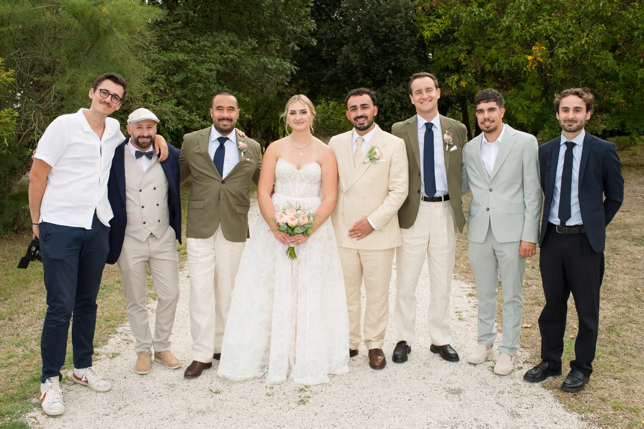 mariés au centre d'une rangée de six hommes en costumes variés dans le parc