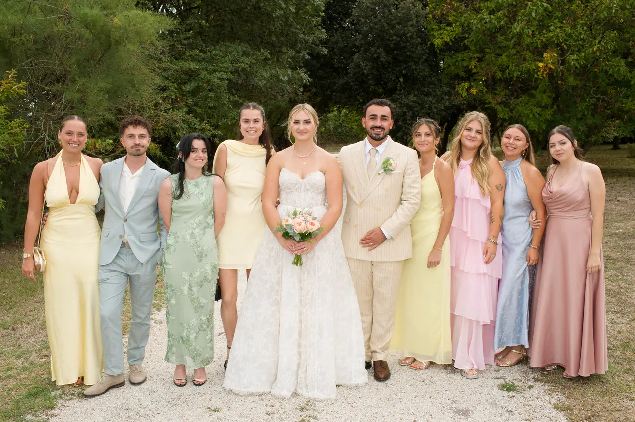 onze personnes en ligne autour des mariés, robes pastel jaune, rose, vert et bleu, gravier