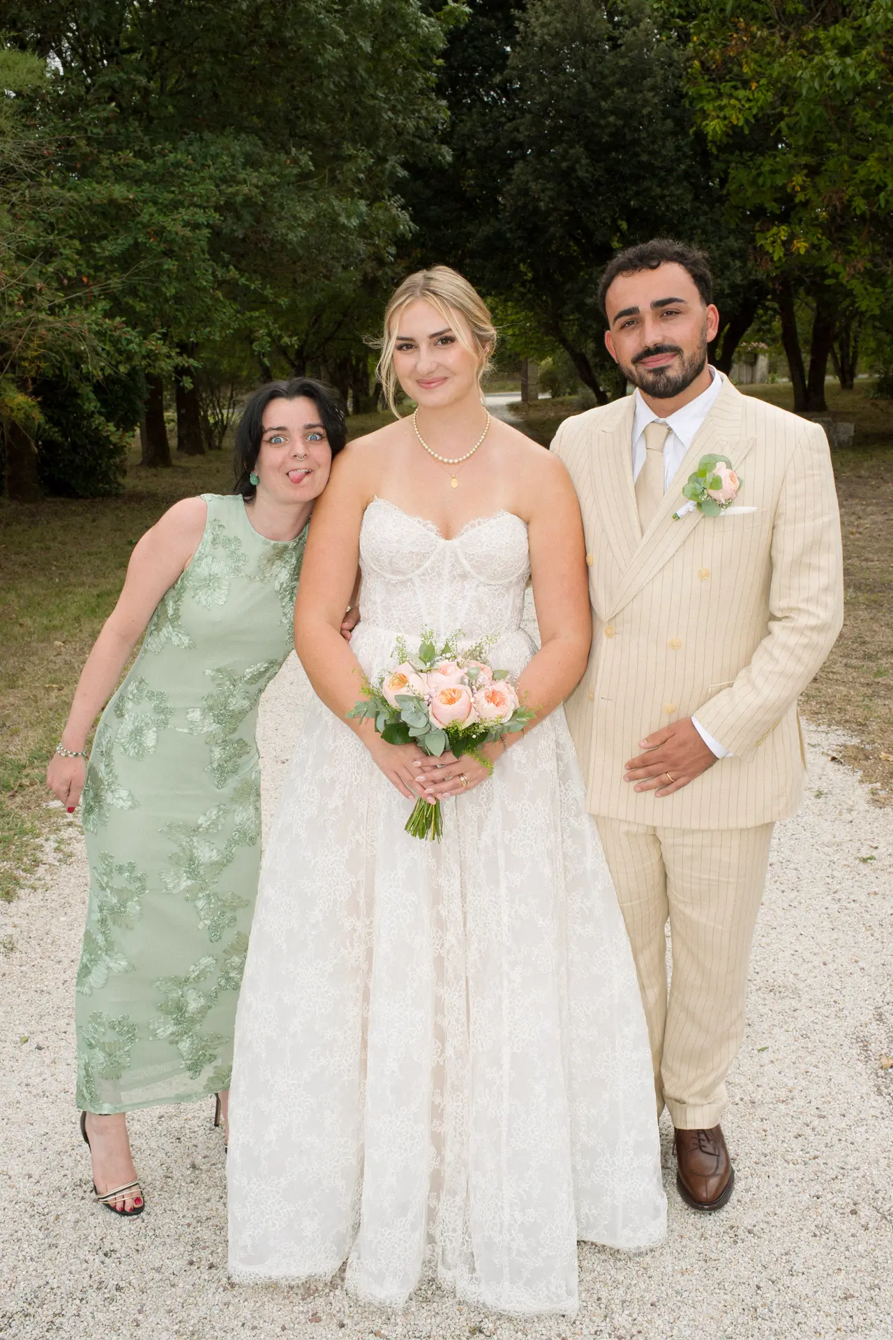 mariés avec une femme en robe verte fleurie tirant la langue, allée du parc