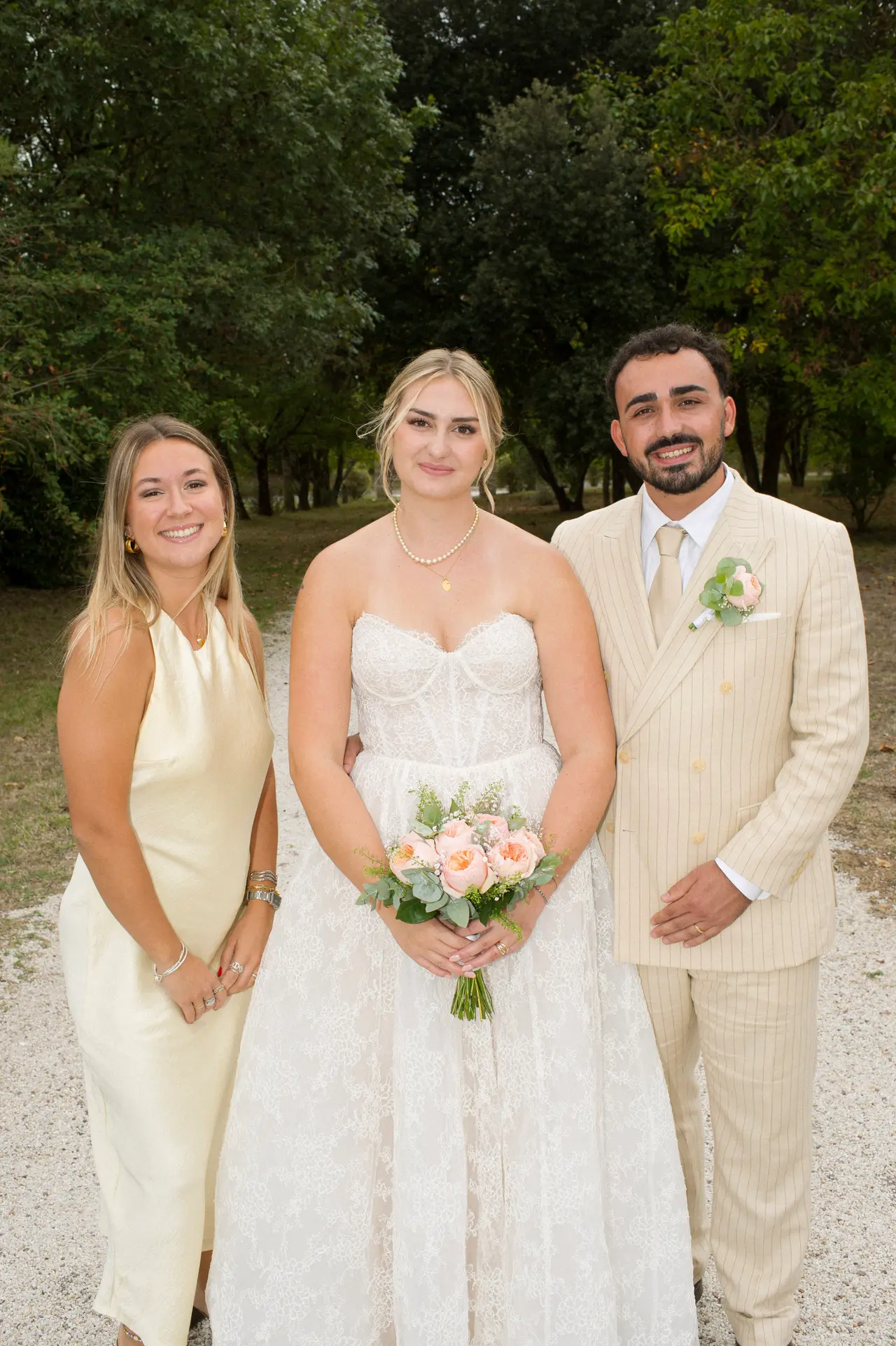 mariés à côté d'une femme blonde en robe satinée crème, allée arborée
