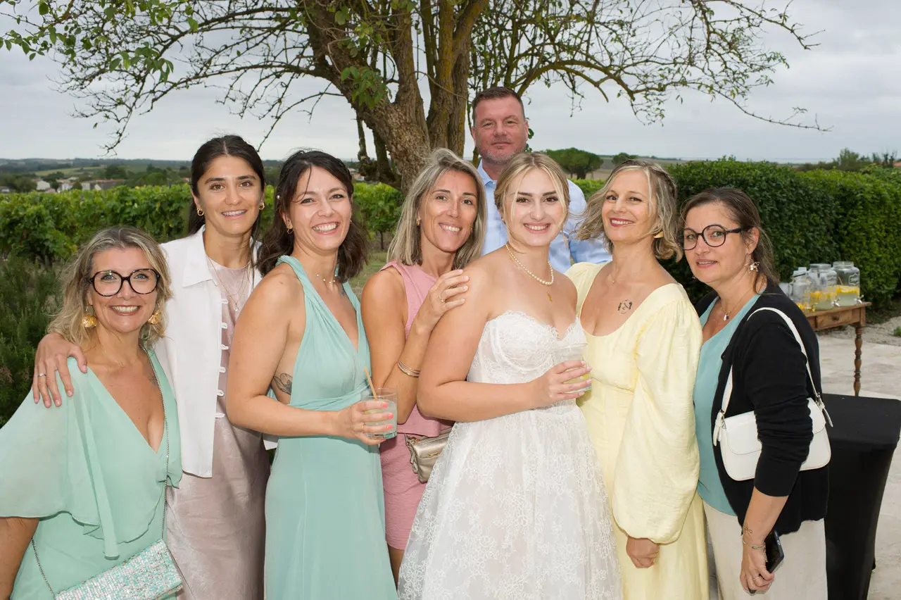 La mariée entourée de six femmes en robes vert d'eau, jaune et rose, sous un arbre